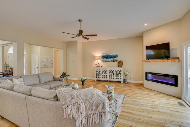 living room featuring baseboards, visible vents, a glass covered fireplace, wood finished floors, and recessed lighting