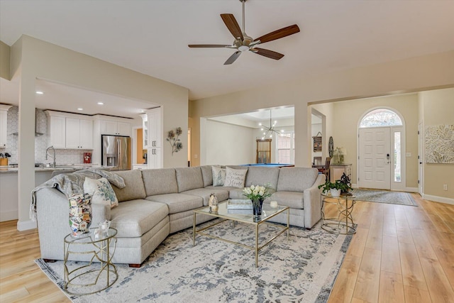 living area with baseboards, light wood finished floors, and ceiling fan with notable chandelier