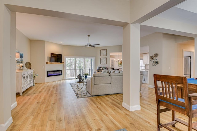 living area with light wood-style floors, baseboards, ceiling fan with notable chandelier, and a glass covered fireplace