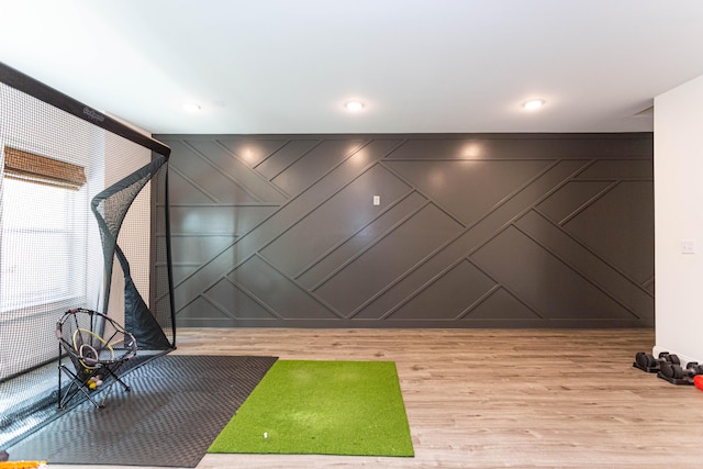 workout room with wood finished floors, a decorative wall, golf simulator, and recessed lighting