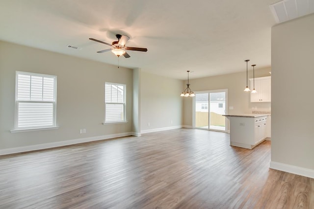 unfurnished living room featuring ceiling fan with notable chandelier and light hardwood / wood-style floors