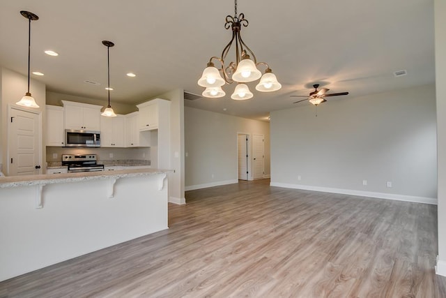 kitchen featuring light stone counters, decorative light fixtures, stainless steel appliances, a kitchen bar, and white cabinets