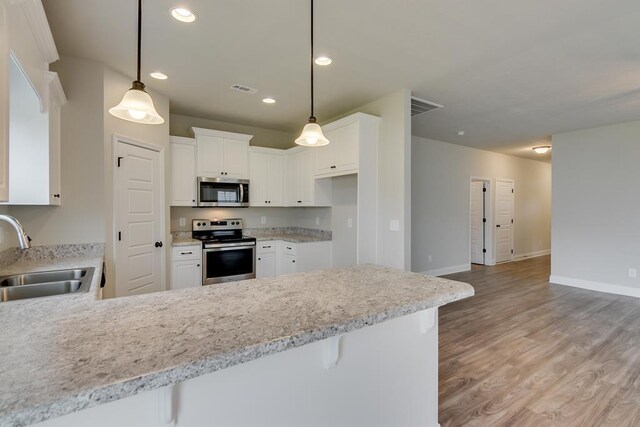 kitchen with a breakfast bar area, stainless steel appliances, light stone counters, white cabinets, and decorative light fixtures