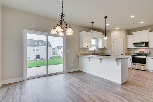 kitchen featuring kitchen peninsula, decorative light fixtures, stainless steel appliances, a kitchen bar, and white cabinetry