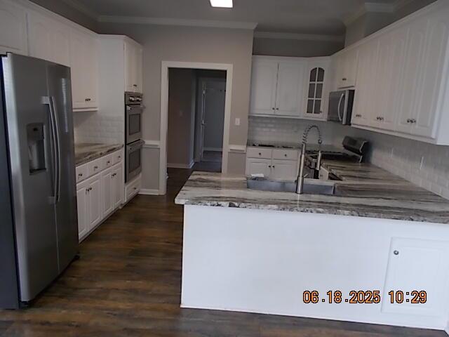 967 Windmill Pkwy, Evans, GA 30809 - kitchen with appliances with stainless steel finishes, a peninsula, crown molding, light stone counters, and glass insert cabinets