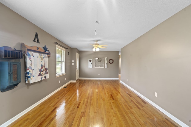 unfurnished living room with a ceiling fan, light wood-style flooring, and baseboards