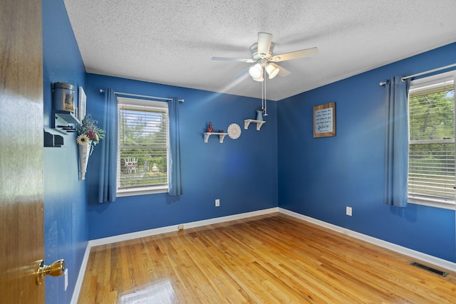 unfurnished room featuring plenty of natural light, ceiling fan, a textured ceiling, wood finished floors, and baseboards