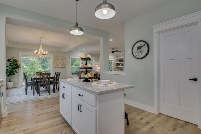 kitchen with ceiling fan with notable chandelier, hanging light fixtures, a kitchen island, light hardwood / wood-style floors, and white cabinetry