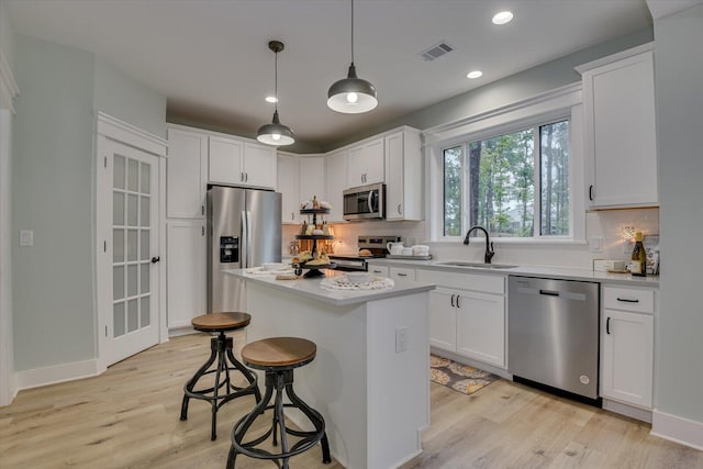 kitchen with appliances with stainless steel finishes, a kitchen island, sink, decorative light fixtures, and white cabinetry