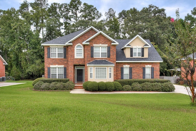 colonial house featuring roof with shingles, brick siding, a front lawn, and cooling unit