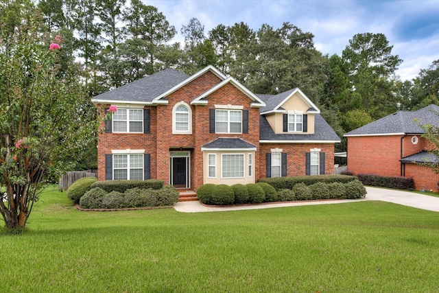 colonial house featuring a shingled roof, a front yard, and brick siding