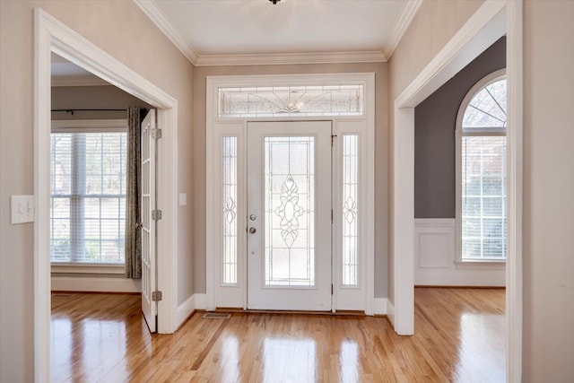 foyer with light wood-style flooring, crown molding, and wainscoting