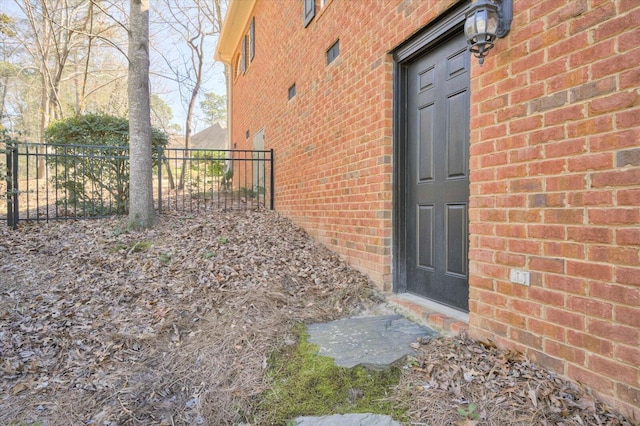 doorway to property featuring brick siding and fence