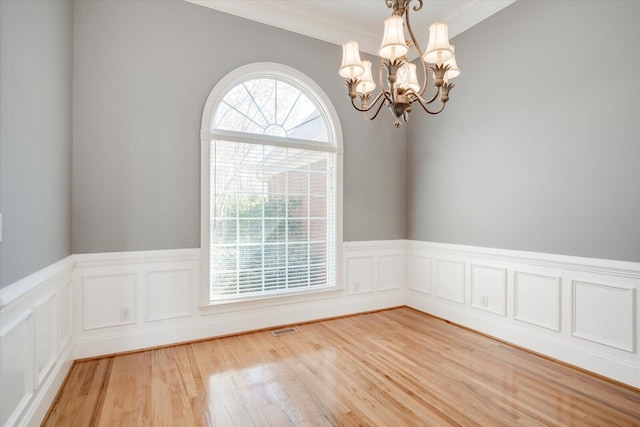 unfurnished room featuring light wood finished floors, visible vents, ornamental molding, wainscoting, and a chandelier