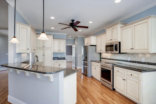 kitchen with a peninsula, appliances with stainless steel finishes, cream cabinetry, and light wood-style floors