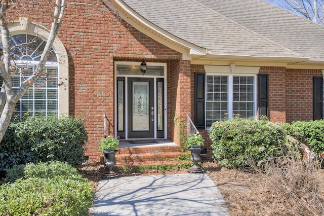 entrance to property featuring a shingled roof and brick siding