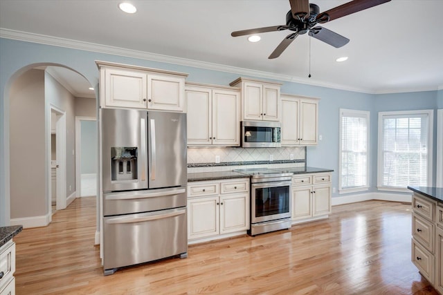 kitchen featuring arched walkways, crown molding, light wood finished floors, decorative backsplash, and appliances with stainless steel finishes