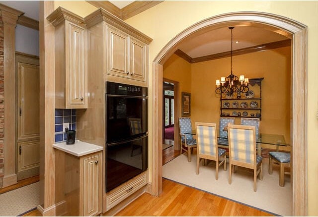 kitchen with black double oven, pendant lighting, a chandelier, light wood-type flooring, and ornamental molding