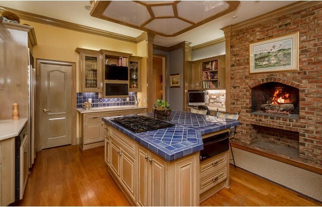 kitchen featuring tile counters, a brick fireplace, light hardwood / wood-style flooring, backsplash, and crown molding