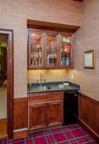 bar featuring black dishwasher, wooden walls, and sink