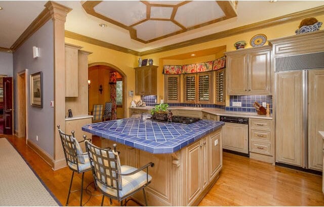 kitchen featuring paneled appliances, light brown cabinets, tile counters, and a breakfast bar area