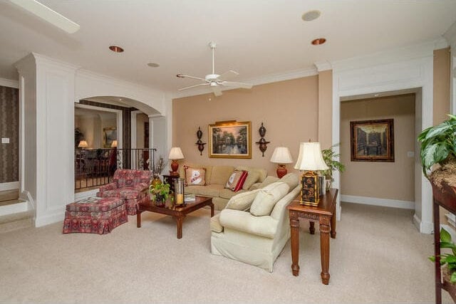 living room with ceiling fan, ornamental molding, and light carpet