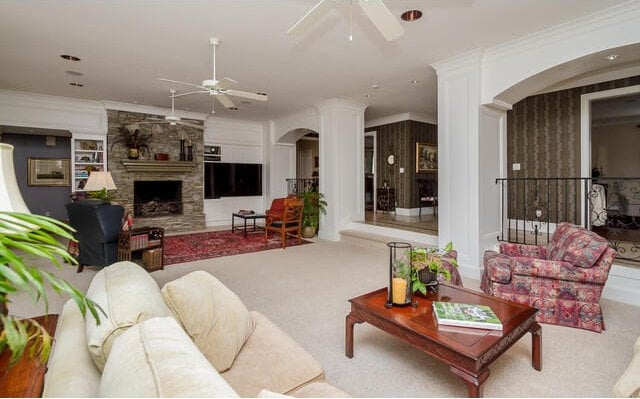 living room with crown molding, light colored carpet, a fireplace, and decorative columns