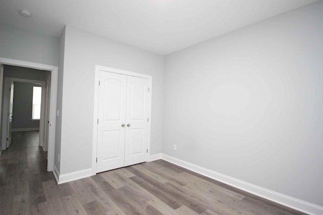 unfurnished bedroom featuring wood finished floors, baseboards, and a closet