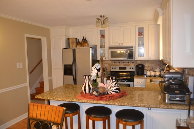 kitchen with light wood-type flooring, light stone countertops, appliances with stainless steel finishes, white cabinetry, and a breakfast bar area