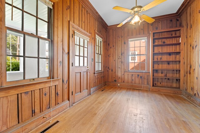 empty room featuring light wood-type flooring, ceiling fan, crown molding, and wood walls