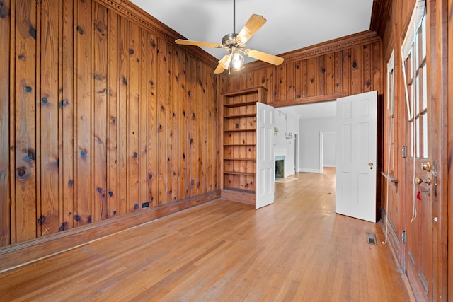 empty room featuring ceiling fan, light wood-type flooring, crown molding, and wooden walls