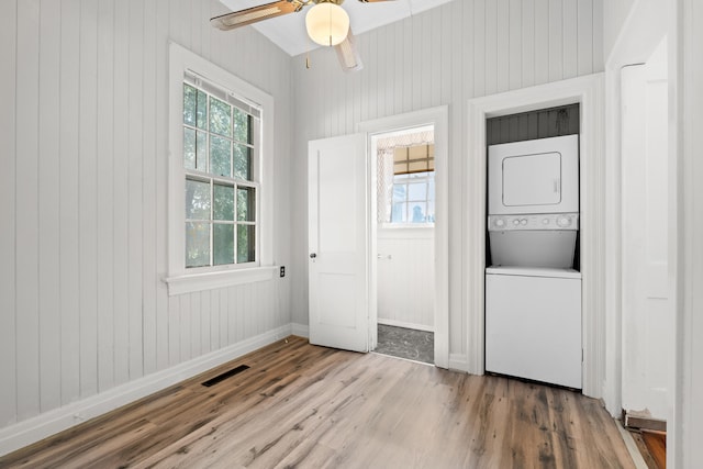 interior space with hardwood / wood-style floors, wood walls, ceiling fan, stacked washing maching and dryer, and ornamental molding