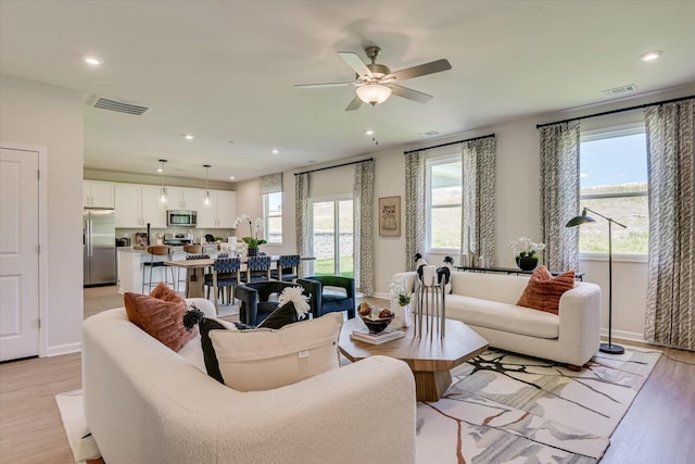 living room with ceiling fan, plenty of natural light, and light wood-type flooring