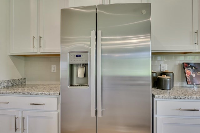 kitchen with light stone countertops, white cabinets, stainless steel fridge, and tasteful backsplash