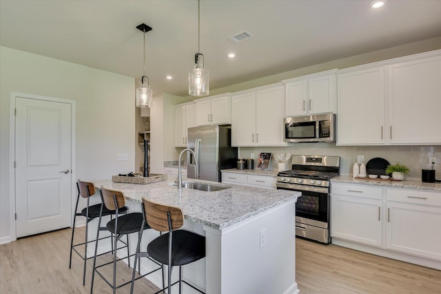 kitchen featuring white cabinetry, stainless steel appliances, an island with sink, sink, and hanging light fixtures