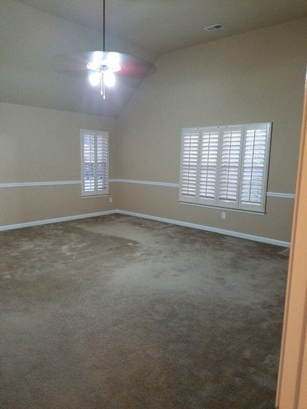 spare room featuring visible vents, carpet flooring, vaulted ceiling, ceiling fan, and baseboards