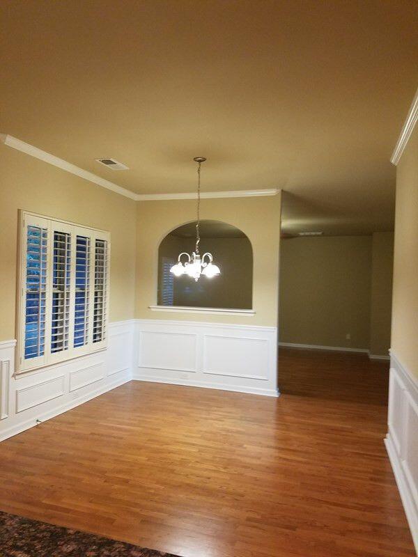 unfurnished room with a chandelier, a decorative wall, wood finished floors, visible vents, and ornamental molding