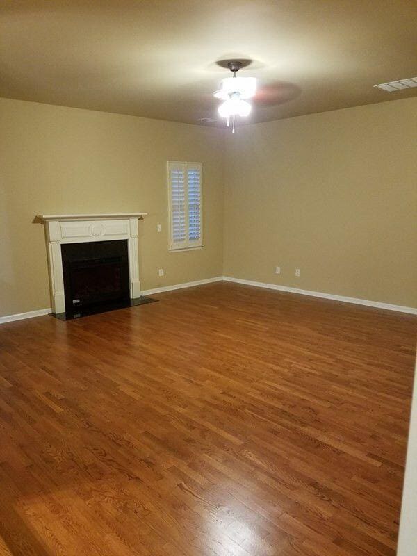 unfurnished living room with wood finished floors, a fireplace with flush hearth, baseboards, visible vents, and a ceiling fan