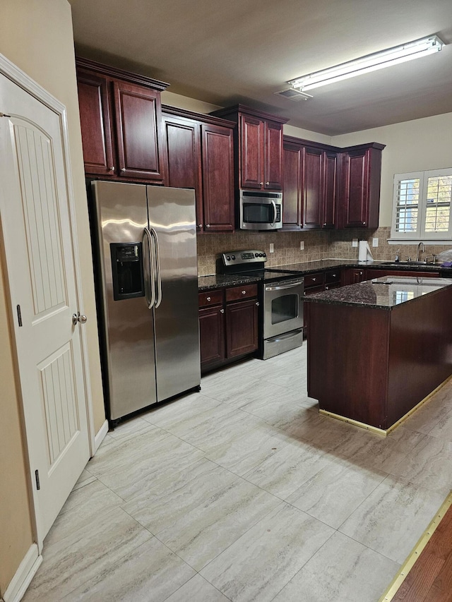 kitchen featuring dark stone counters, stainless steel appliances, dark brown cabinets, and backsplash