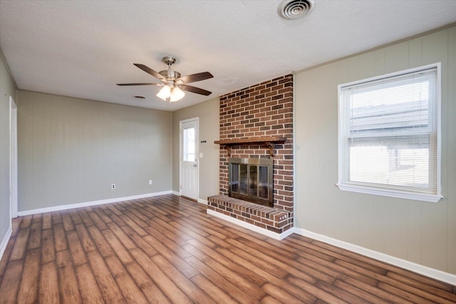 unfurnished living room with hardwood / wood-style flooring, ceiling fan, a brick fireplace, and a textured ceiling