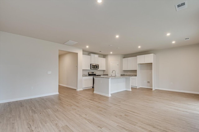 kitchen featuring an island with sink, white cabinets, light stone counters, light hardwood / wood-style floors, and stainless steel appliances