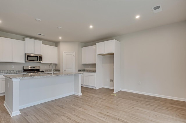 kitchen featuring light stone counters, stainless steel appliances, a center island with sink, and white cabinets