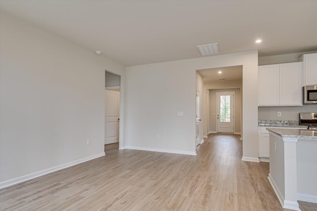 kitchen with white cabinetry, light stone countertops, range, and light hardwood / wood-style flooring