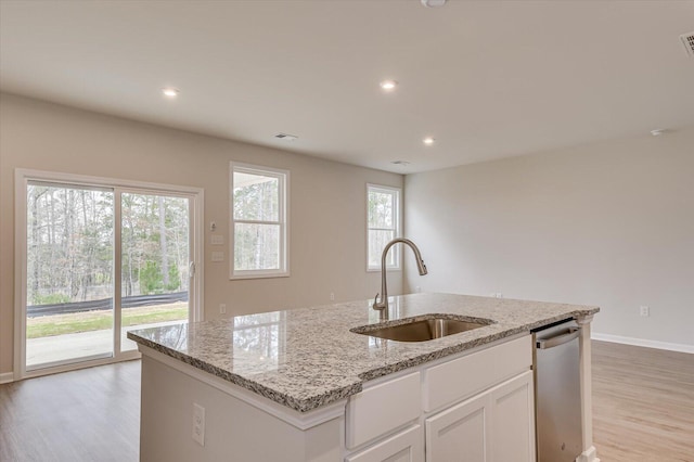 kitchen with sink, stainless steel dishwasher, an island with sink, light stone countertops, and white cabinets