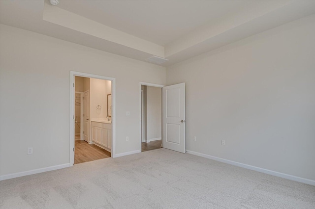 unfurnished bedroom featuring light colored carpet, a tray ceiling, and ensuite bath