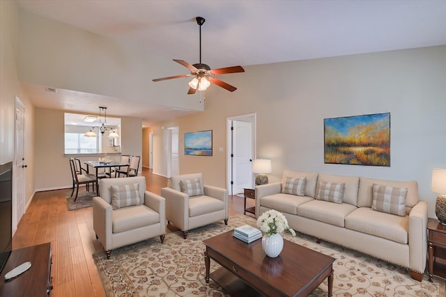 living area with light wood-style flooring, visible vents, baseboards, high vaulted ceiling, and ceiling fan with notable chandelier