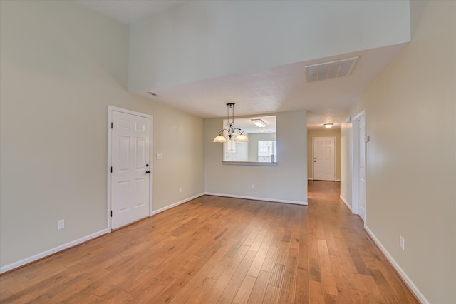 spare room with light wood-type flooring, visible vents, a notable chandelier, and baseboards