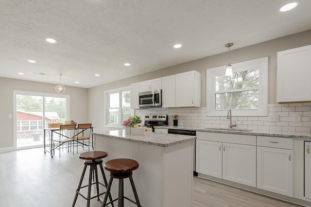 kitchen featuring hanging light fixtures, stainless steel appliances, a center island, light stone counters, and white cabinets