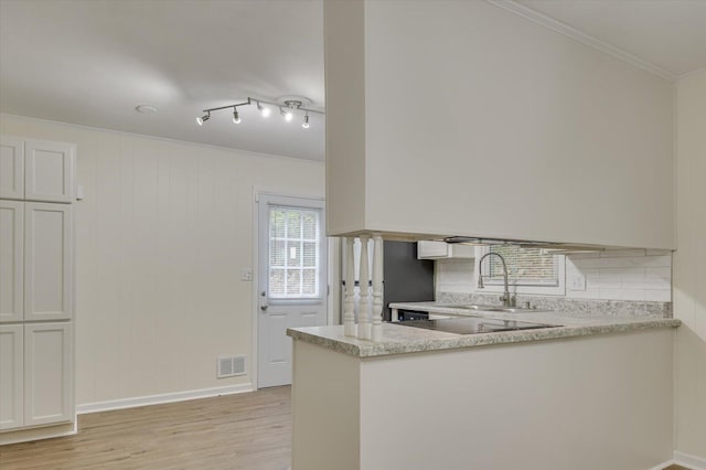 kitchen with light wood-type flooring, ornamental molding, a peninsula, visible vents, and a sink