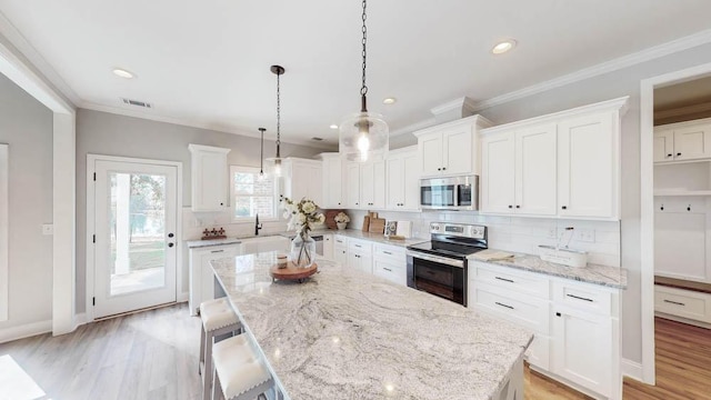 kitchen featuring stainless steel appliances, white cabinetry, a center island, and decorative light fixtures